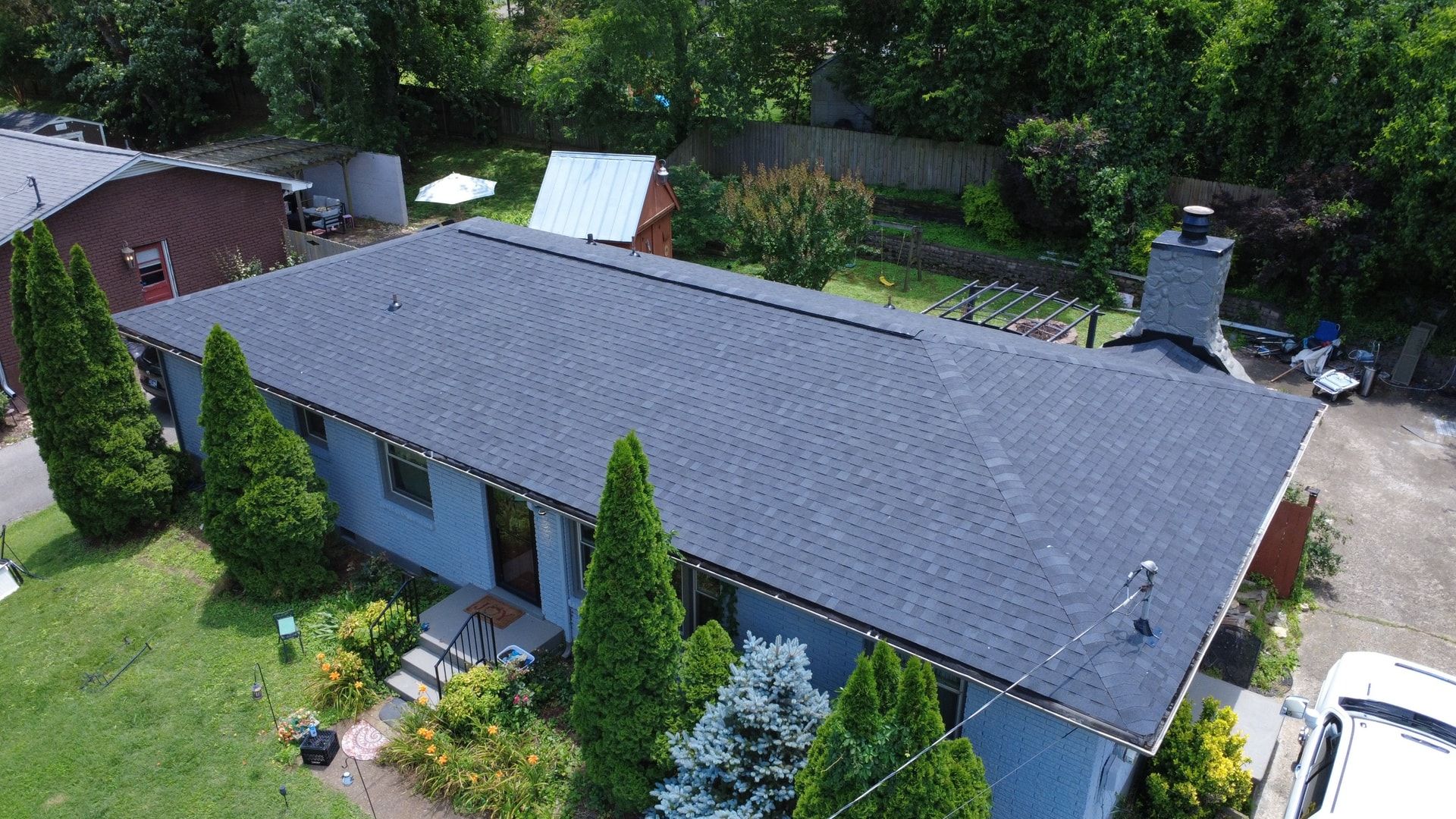 Aerial view of a single story blue brick home with a new charcoal shingle roof and a stone chimney after replacement