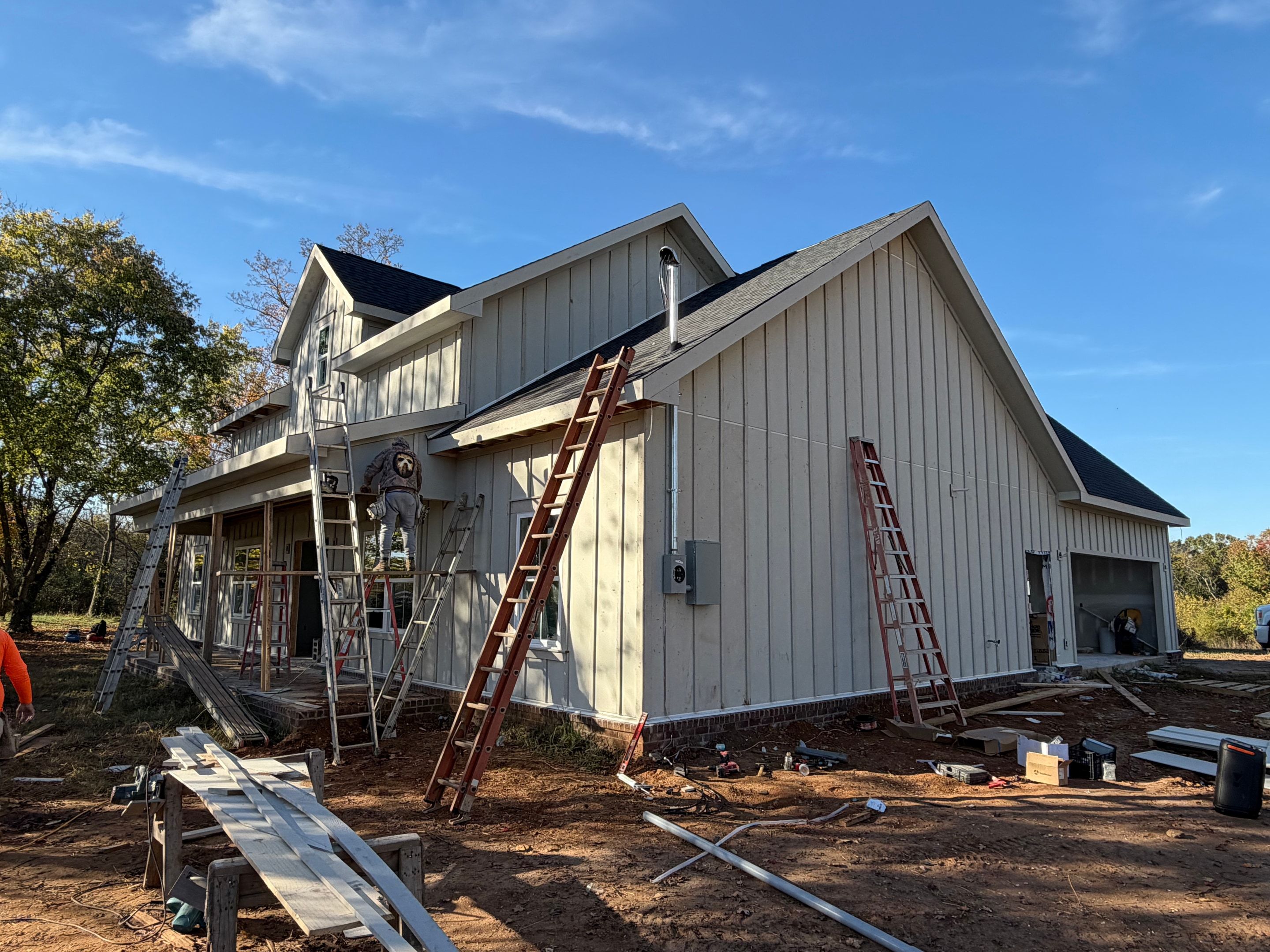 Crew on ladders installing vertical board and batten siding on a new two story home with a dark shingle roof under a blue sky
