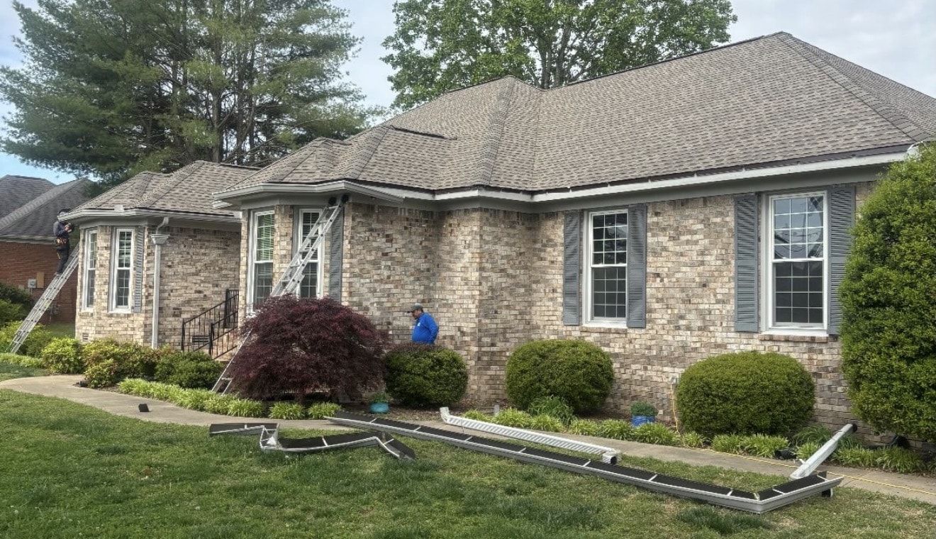 Single story brick home with new seamless gutter sections staged on the lawn during installation