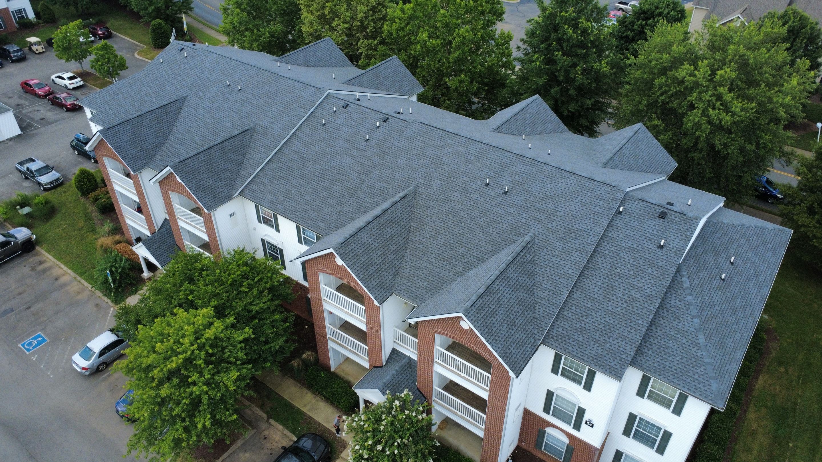 Aerial photo of new charcoal architectural shingles on a multi building brick and siding residential property, with dormers and ridge lines visible